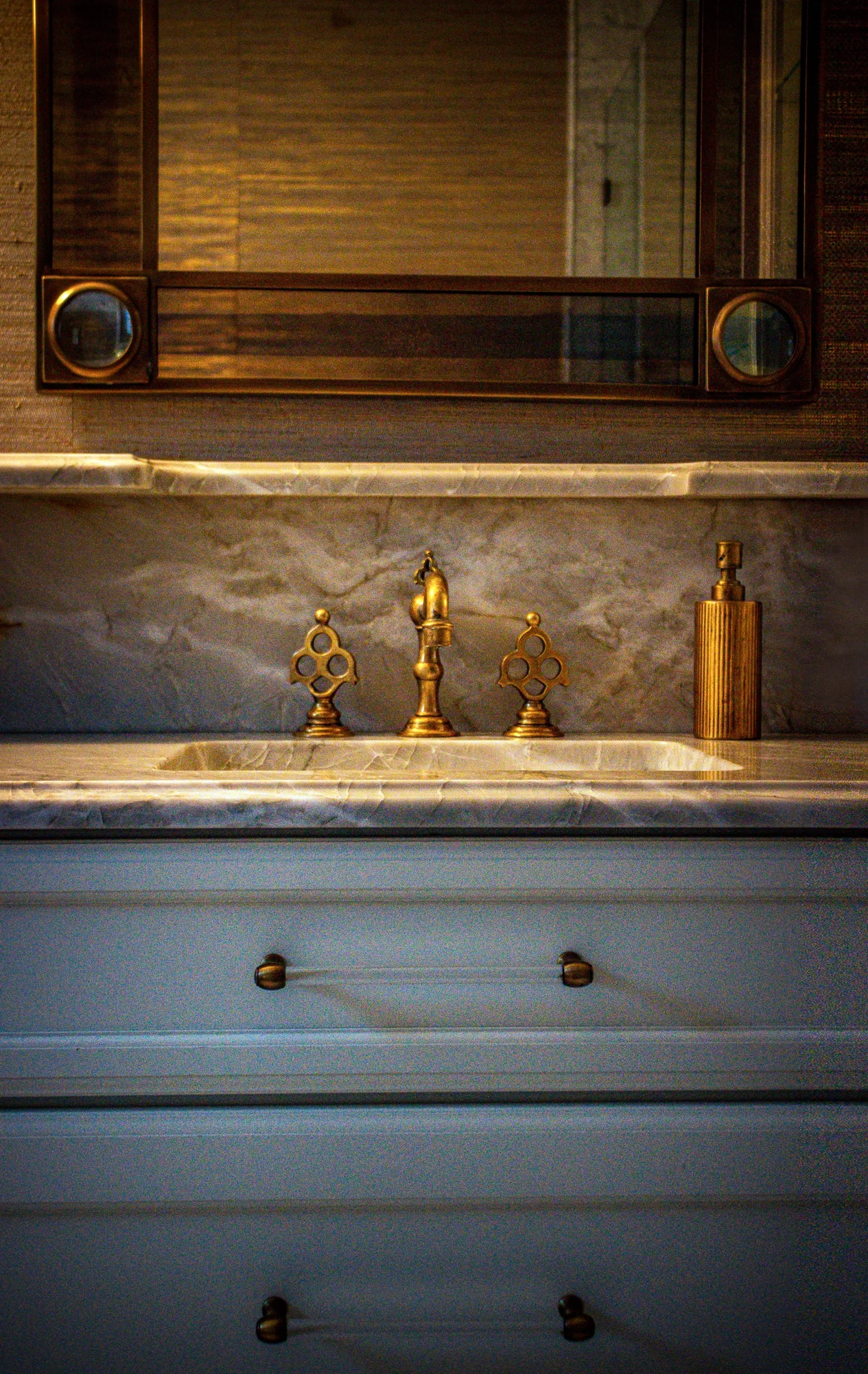 Painted vanity cabinetry and expressive stone beneath a framed mirror at Ashland Park